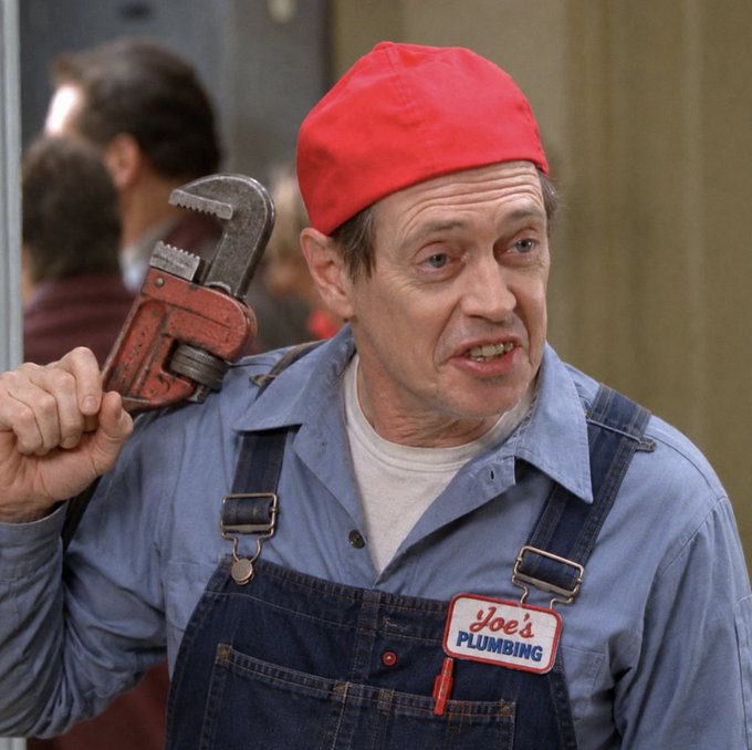 An older man wearing a red cap and denim overalls with a 'Joe's Plumbing' name tag holds a pipe wrench over his shoulder with a grimacing expression.