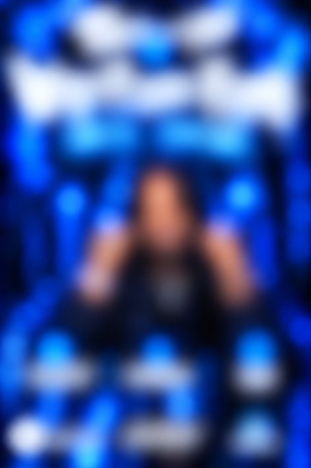 A heavily blurred image of a person wearing a dark shirt against a blue background with light patterns.