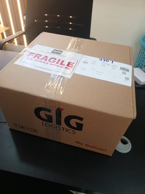 A cardboard shipping box labeled "GIG LOGISTICS" with "FRAGILE" and "HANDLE WITH CARE" stickers sits on a dark table.