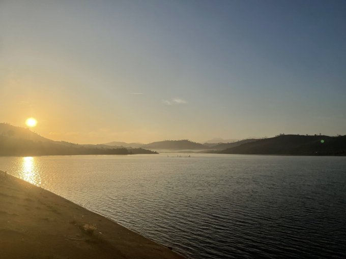 A serene sunset over a calm lake with mountains in the background, the sun low on the horizon casting golden light across the water.