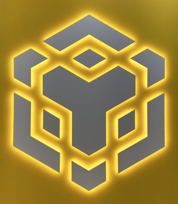 A glowing BNB logo featuring its geometric cube emblem in gray with radiant yellow-orange outlines is displayed, symbolizing the strength and vibrancy of the #BNB community in Web3.