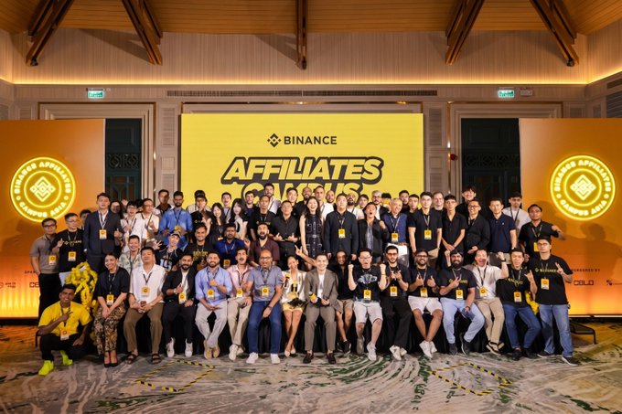 A large group of attendees, many wearing Binance-branded shirts, pose together on stage at the "Binance Affiliates Campus" event in Asia, captured during Day 2 of the conference. The image showcases the community and networking highlighted in the post's message about "more conversations, more learning, more connections."