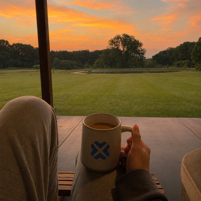 Relaxing on a porch with a coffee mug, taking in a stunning sunset over a green field to greet the morning.