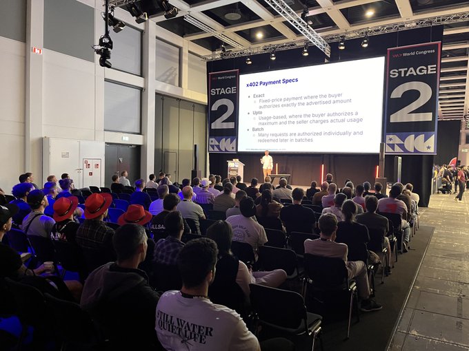 A speaker presents on Stage 2 at WeAreDevs World Congress, with a slide titled "x402 Payment Specs" detailing Exact, Split, and Batch payment authorizations for the Algorand blockchain, while an audience of developers listens attentively. The image captures the conference talk referenced in the post, where Algorand's Sr. Director of Integrations & Dev Tooling discusses how x402 and Algorand enable agentic commerce.