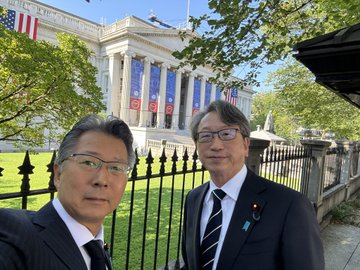 Two men in dark suits pose for a photo in front of a stately neoclassical building with columns and American flags, suggesting an official diplomatic or policy meeting. Given the post's reference to Japan's stablecoin policy, the image likely represents Japanese representatives visiting a U.S. financial or governmental institution to discuss stablecoin regulations and cross-border digital currency collaboration.