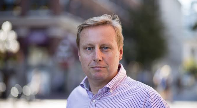A middle-aged man with short blonde hair and a serious expression stands outdoors, wearing a white and blue striped button-up shirt against a blurred urban backdrop. The image relates to the caption by showing Marc van der Chijs, co-founder of Bitcoin mining company Hut 8, who has shifted his capital toward AI while still advocating for Bitcoin as a worthwhile holding.