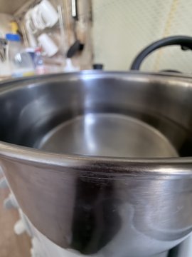 A close-up view shows a large empty stainless steel mixing bowl sitting on a kitchen counter, with utensils and a paper towel roll visible in the background.