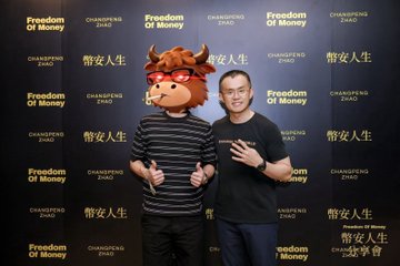Two men posing together in front of a step-and-repeat backdrop for 'Changpeng Zhao: Freedom of Money,' with one person wearing a mascot head.
