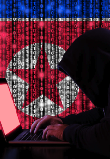 A hooded figure types on a laptop displaying binary code overlaid with the North Korean flag, symbolizing the cyber activities attributed to the Lazarus Group. The image visually represents the recent alert that North Korea-linked wallets transferred $30 million in crypto through Hyperliquid, converting Bitcoin into ETH or SOL before depositing funds into major exchanges like KuCoin, Kraken, and LBank.
