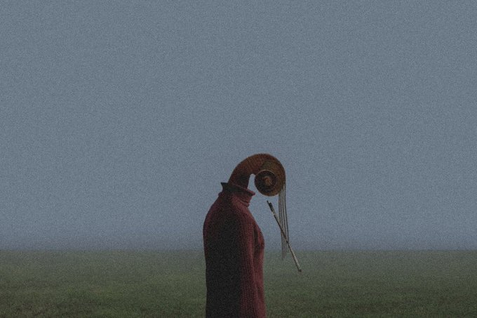 A moody, atmospheric image of a figure in a maroon cloak with a long curved horn on their head, standing in a misty field under a gray sky, holding arrows.