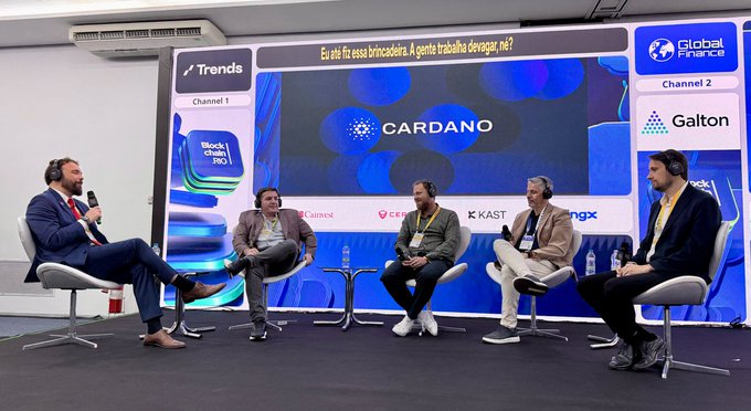 Five men sit on a panel stage at an event branded "Global Fintech Fest" with the "CARDANO" logo prominently displayed on the screen behind them.