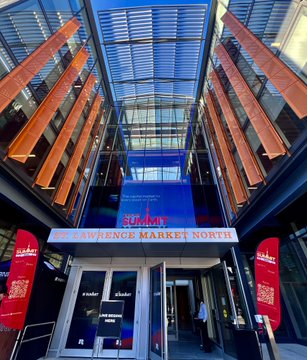 The entrance to the 'LAWRENCE MARKET NORTH' building, featuring a red and blue sign, glass atrium, and red banners with QR codes.