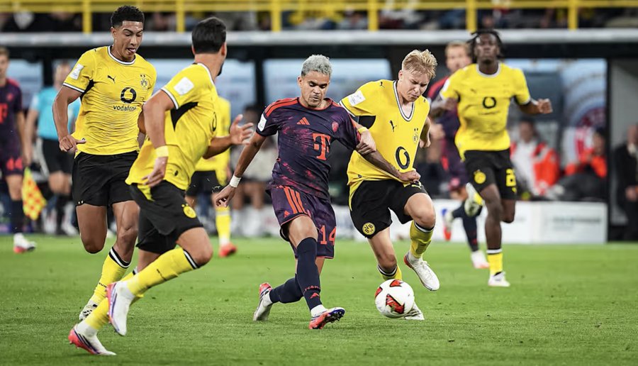 A soccer match action shot showing Bayern Munich player #14 (Luis Díaz) dribbling the ball while surrounded by Borussia Dortmund defenders in their yellow and black kits.