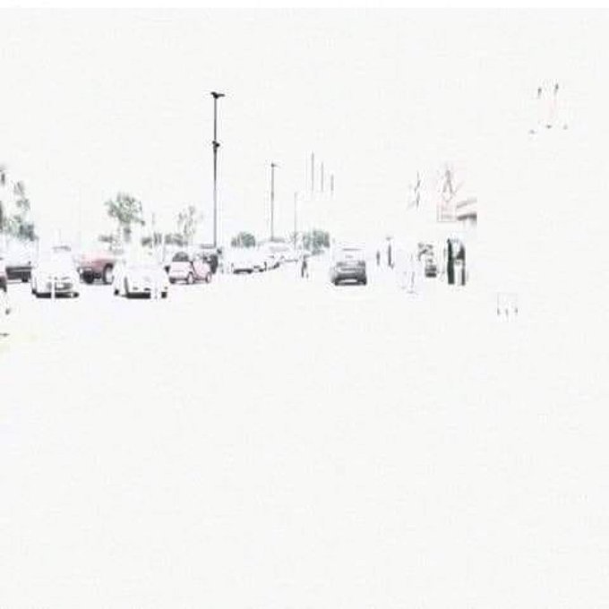 A faded, washed-out photograph of a parking lot with cars and street lights, where the upper and right portions of the image appear to have been erased or overexposed to white.