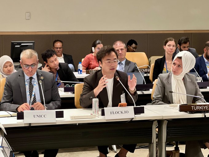 The image shows Flock.io's founder and CEO speaking at a panel discussion at UN Headquarters, seated between representatives from UNICC and Türkiye, with delegates from various countries visible in the background. This visual directly supports the post's message about showcasing blockchain and decentralized AI solutions for public systems at the UN.

Visible signage includes placards reading "UNICC," "FLOCK.IO," and "TÜRKIYE."