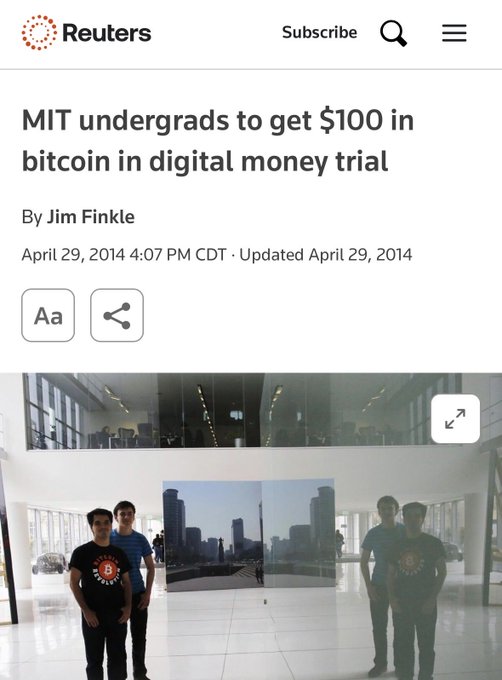 The image shows a Reuters article from April 29, 2014 titled "MIT undergrads to get $100 in bitcoin in digital money trial" by Jim Finkle, featuring a photo of two students standing in a modern building lobby. The article relates to the accompanying post about the MIT bitcoin giveaway, where the pictured students likely represent the organizers who distributed the cryptocurrency trial to undergraduates.