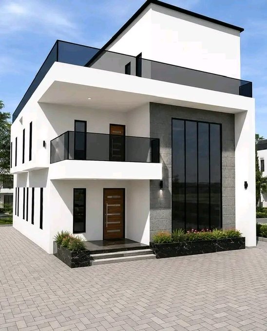 A modern, two-story white and gray residential house with large dark-tinted windows, glass balcony railings, and a paved driveway.