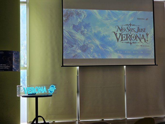 A presentation or conference room setup featuring a large screen displaying a 'No Sus, Just Verona!' advertisement with a Renaissance-style figure against a blue sky, and a glowing neon 'VERONA' sign on a stand below.