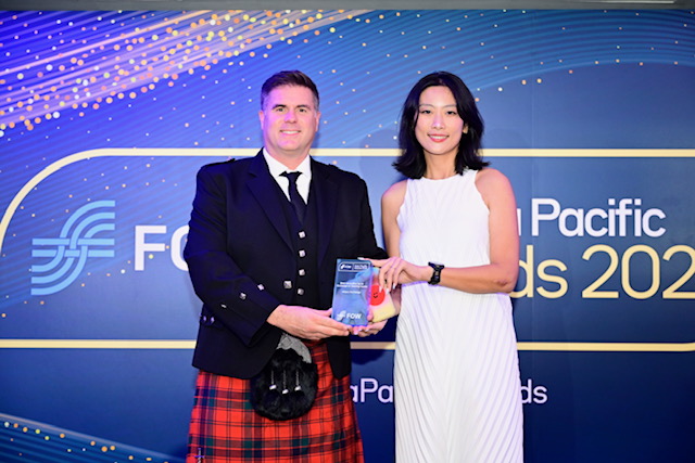 A photo from the Asia Pacific Brands 2024 awards ceremony showing a man in traditional Scottish attire (kilt and sporran) presenting an award to a woman in a white sleeveless dress.