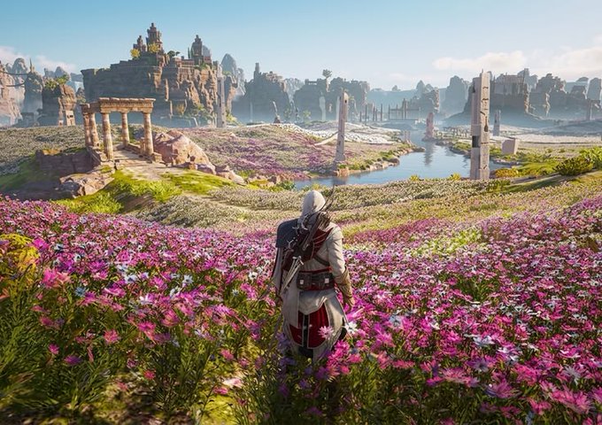 The image features an Assassin's Creed game character standing in a field of purple flowers with mountains in the background. The character appears to be looking at something off-camera, possibly observing their surroundings or focusing on a specific point of interest. The scene is set against a backdrop of a beautiful landscape that includes mountains and a river, creating a serene atmosphere for the game character's adventure.