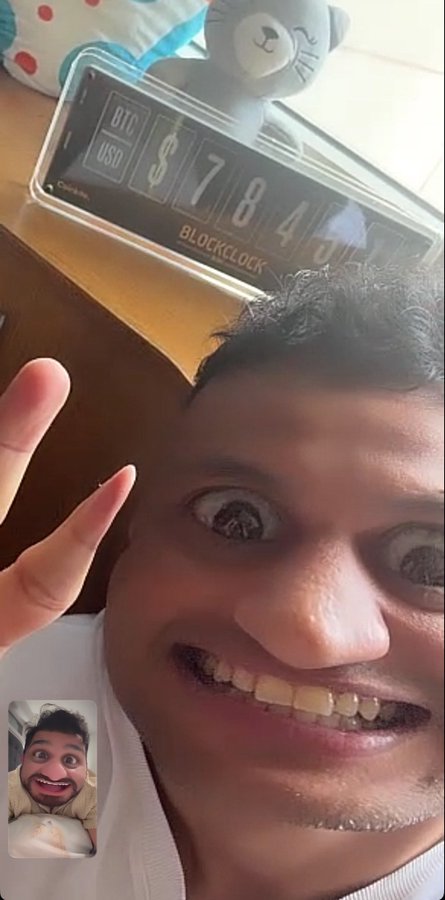 A young man makes an exaggerated wide-eyed expression and flashes a peace sign beside a "BLOCKCLOCK" device displaying BTC USD prices ($784+...), reacting with comedic shock to the Bitcoin price shown. The small inset in the corner shows a puppet filter version of himself, matching the post's playful tone about the crypto price.