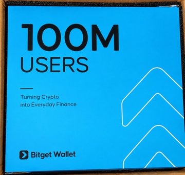A blue Bitget Wallet promotional package is displayed with bold "100M USERS" text and the tagline "Turning Crypto into Everyday Finance." This is the 8th anniversary gift commemorating Bitget Wallet's milestone of reaching 100 million users, as celebrated in the accompanying post.