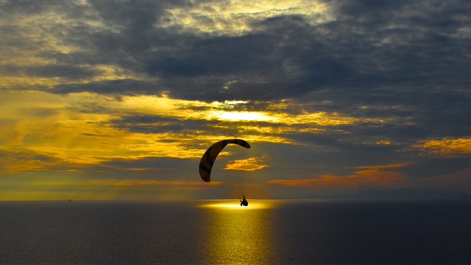 iced water and a parasailer silhouetted against a vibrant sunset sky, with the parasailer's silhouette appearing as a dark line.