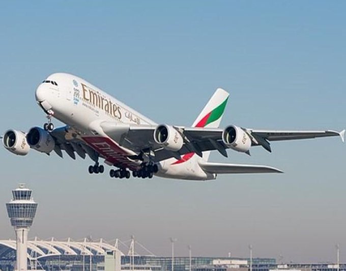 An Emirates Airbus A380, identifiable by the "Emirates" branding and UAE flag colors on its tail, takes off from an airport, illustrating the airline referenced in the announcement about accepting Bitcoin and other cryptocurrencies as payment for flights through its app.