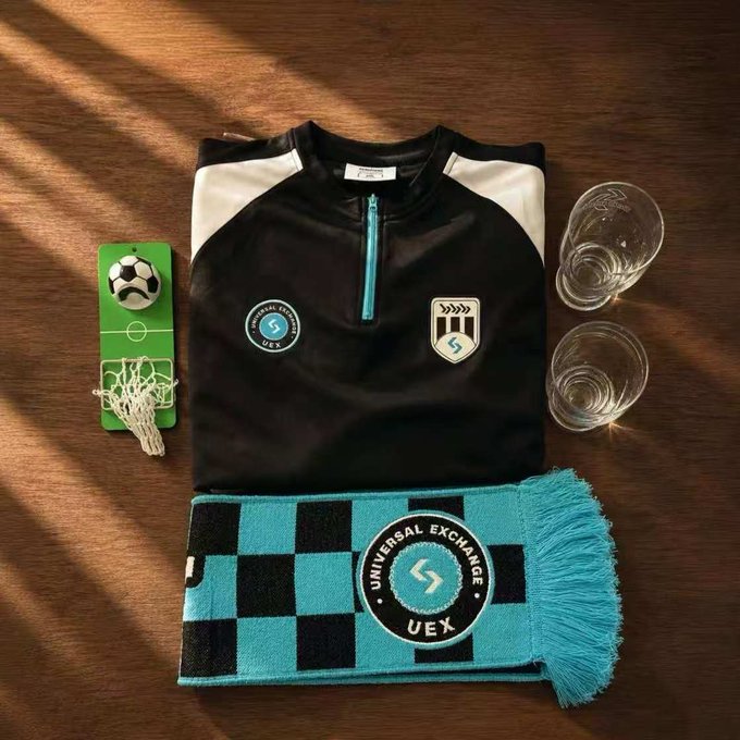 The image features a black and white soccer jersey, a blue scarf with a logo, and two glasses of water placed on a wooden table. The objects are arranged in a way that suggests they might be part of a gift set or a promotional display for Universal Exchange.