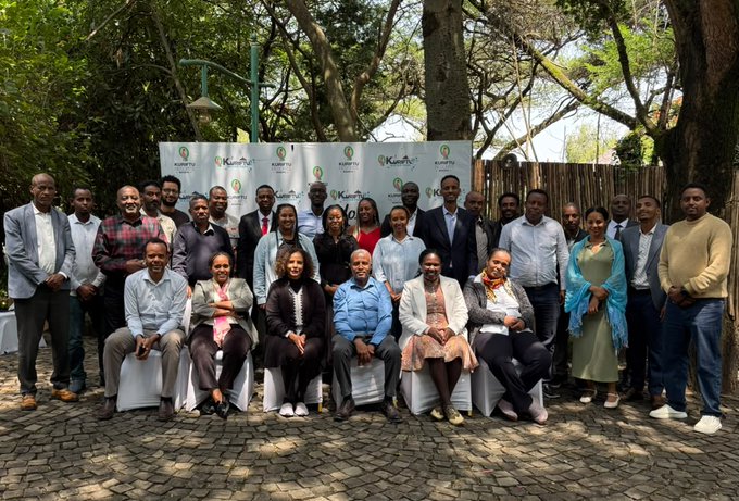 A large group of people poses for a formal group photo outdoors in front of a banner displaying the 'Kenyatta University' logo.