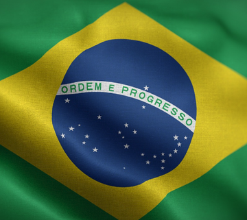 The Brazilian flag waves prominently, featuring its iconic green field, yellow diamond, and blue celestial globe inscribed with the national motto "Ordem E Progresso." This image directly relates to Brazil's central bank regulatory action, symbolizing the nation imposing new restrictions on cryptocurrency withdrawals through Resolution 584.