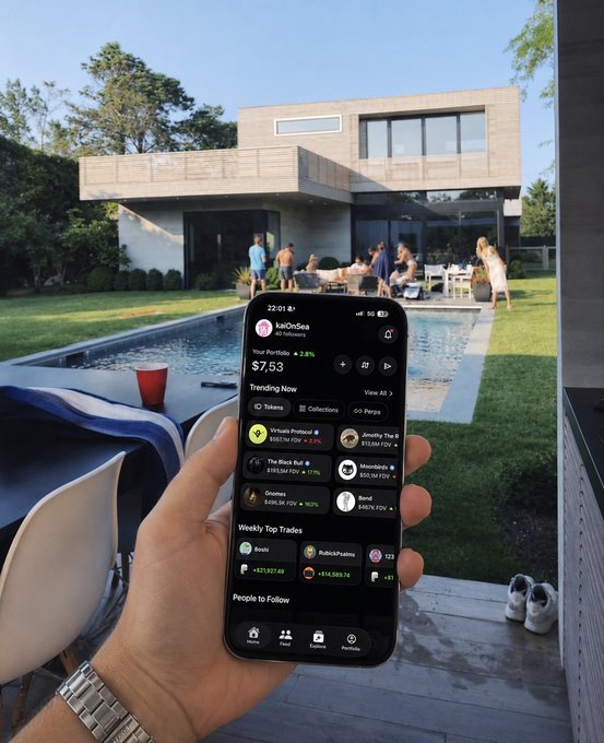 A first-person view of a hand holding a smartphone displaying a crypto portfolio app called 'kaoOnSna' showing a balance of $7.53, with a pool party and modern house in the background.