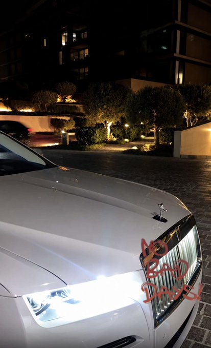 The front of a white luxury car with headlights illuminated is shown at night, with the text 'NO BAD DAYS' written in red on the hood.
