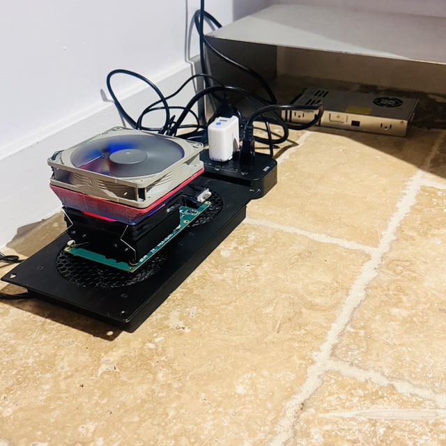 A disassembled NerdQAxe++ ASIC Bitcoin miner setup sits on a tiled floor, showing exposed internals with a large cooling fan, circuit board, and power supply connected via cables. The image illustrates the user's overclocked mining rig running at 6.5, producing approximately 1 DGB (DigiByte) per day as referenced in the post.