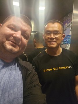 Two men smile for a selfie, with one wearing a t-shirt that reads 'EXCHANGE THE WORLD' in reverse.
