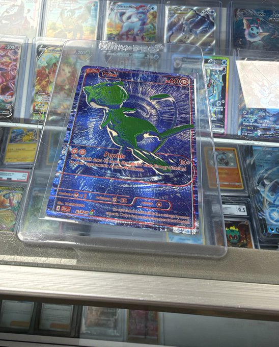 A holographic green Charizard Pokémon card encased in a protective plastic sleeve, resting on a glass display case filled with other graded cards.