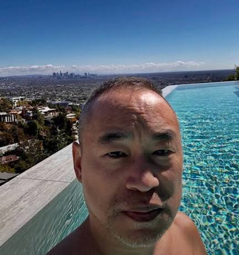 A selfie of a man in front of an infinity pool with a city skyline visible in the background.