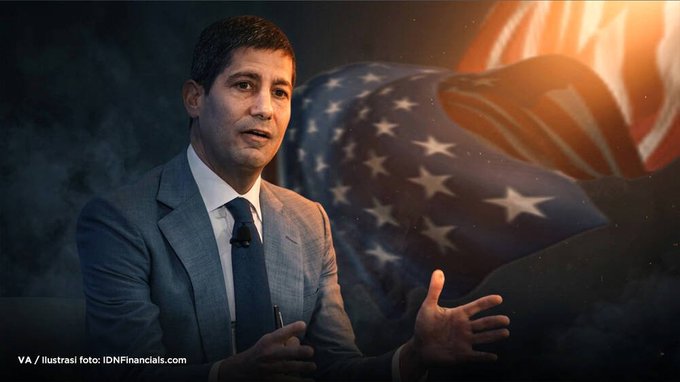 A man in a gray suit speaking, superimposed over an American flag with text reading 'VA / ilustrasi foto: IDNFinancials.com' in the corner.