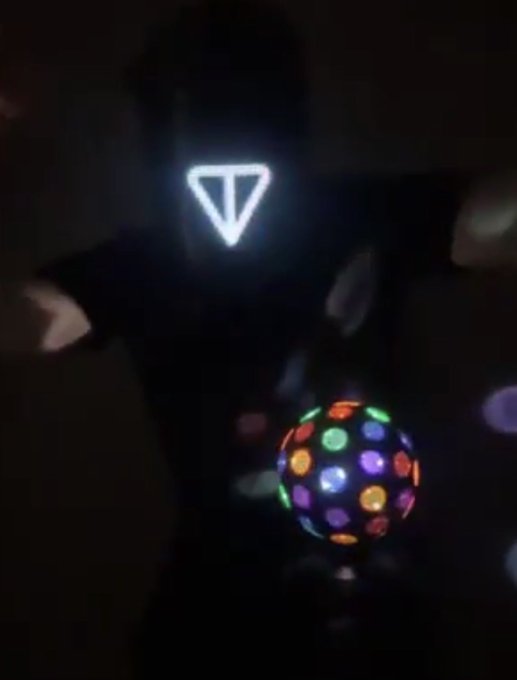 The image features a person wearing a mask with a triangle design, standing against a dark background. In front of them, there's a colorful disco ball that reflects light from various angles, creating a vibrant display. The caption "Happy Birthday $TON" is written in white text at the bottom right corner of the photo.