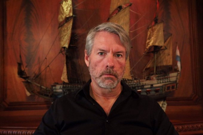 Michael Saylor, the Bitcoin advocate and MicroStrategy co-founder, is pictured with a serious expression in front of a model ship and painting. The image accompanies news of his newly published 755-to-953-hour suggested reading curriculum, which spans history, economics, and technology before culminating in Bitcoin.