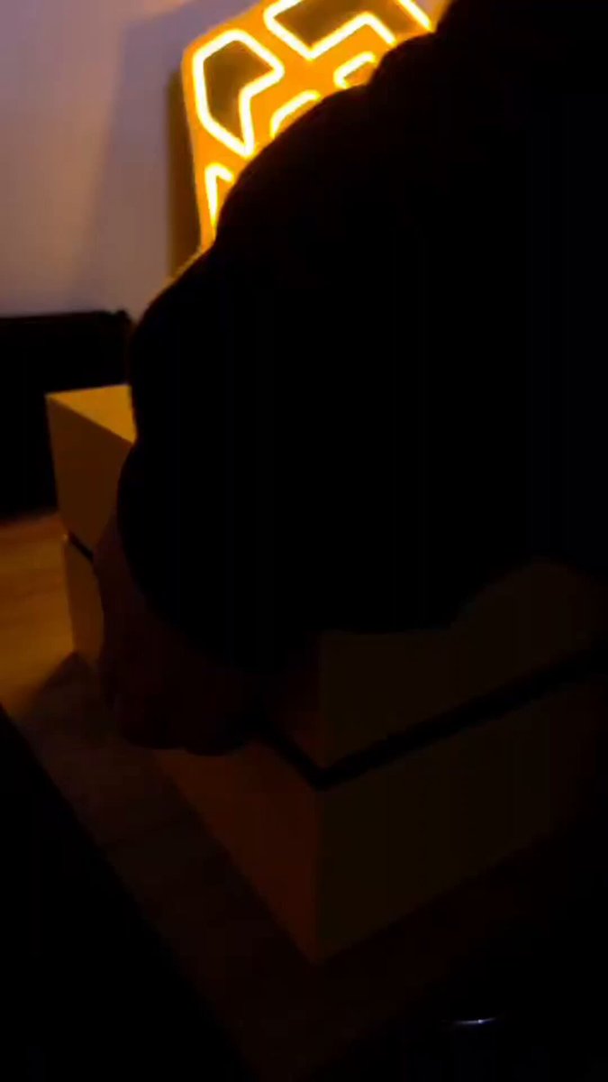 The image features a person sitting at a table with two boxes, one yellow and one black. The person's shadow can be seen on the wall behind them, adding depth to the scene. The text "Finally, my Builder'S Box from BNB Chain arrived A small recognition for years of work building, connecting communities, and bringing Web3 to more people." is present in the image as well.