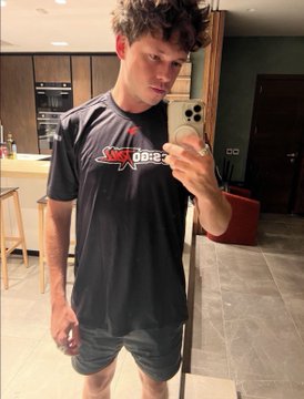 A young man takes a mirror selfie in a modern kitchen, wearing a black t-shirt with reversed "CSGORoll.com" branding visible on the chest. The image likely depicts one of the individuals named in the accompanying post—Killian McKeon Eccles or Daniel Robert Dixon, both linked to CSGODiamonds/CSGORoll and the flagged 164 BTC transaction.