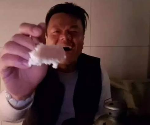A close-up of a man with a strained expression holding up a small, chewed piece of food toward the camera.