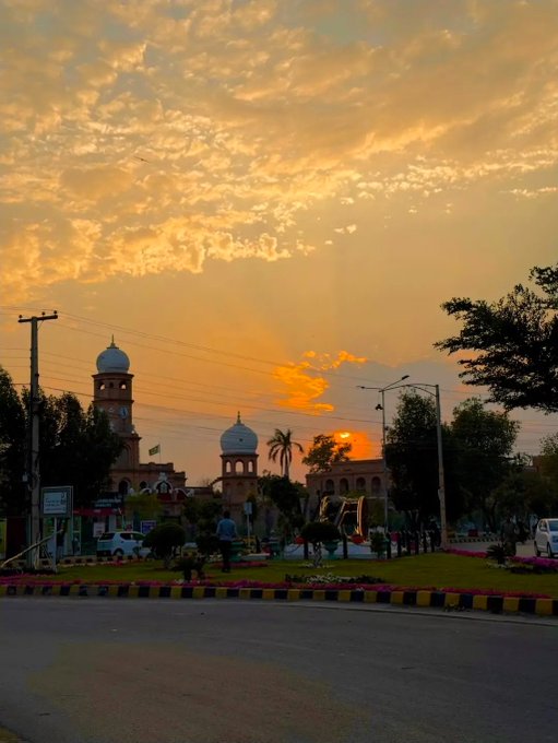 A sunset view of a city street featuring a building with distinctive blue-domed towers and a flag, likely a historic site, under a cloudy orange sky.