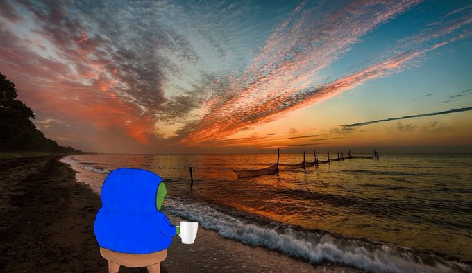 A blue cartoon character with a green face sits on a small stool at the edge of a beach, holding a white mug while watching a vibrant sunset over the ocean.