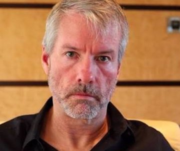 A portrait of a bearded man with graying hair, wearing a dark shirt against a wood-paneled background, illustrates the post about Michael Saylor's advocacy for Bitcoin adoption and the U.S. Senate's potential advancement of the CLARITY Act to establish clearer crypto regulations.