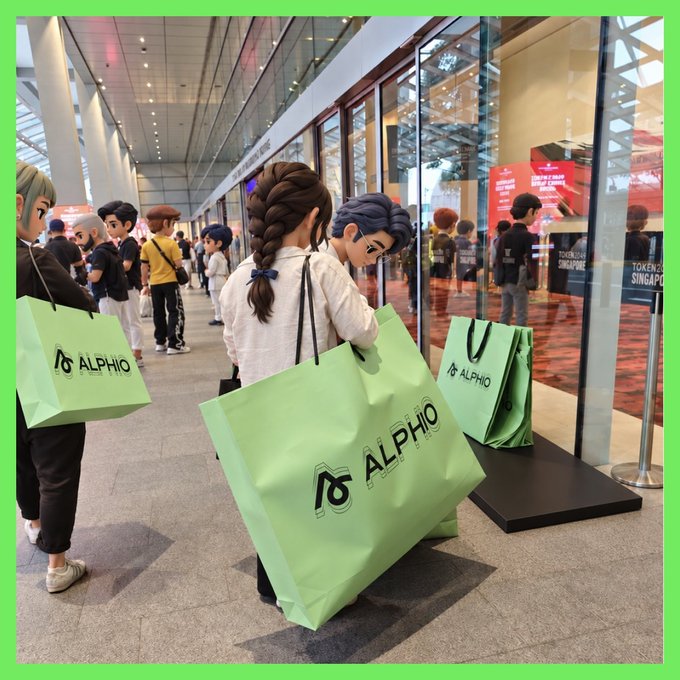 The image shows life-sized animated character figures carrying large green "ALPHIO" branded shopping bags in what appears to be a convention center or trade show venue, with "TOKEN2049 SINGAPORE" visible on signage in the background. The accompanying post mentions Alphio's social feed feature for tracking traders' transactions, and the image cleverly illustrates this concept by depicting characters visibly "showcasing" their Alphio purchases—mirroring how users on the platform can view and follow others' trading activity.