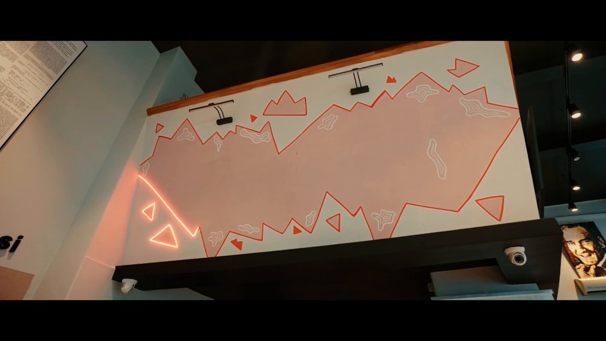 The image features a large white wall with an abstract painting depicting mountains and triangles. The painting has been done using neon paint, giving it a vibrant and eye-catching appearance. The text "We celebrated the tastiest milestone in the crypto world together! At our Crypto Friday event, organized in collaboration with @altcointurk on Bitcoin Pizza Day" is written above the painting, indicating that this artwork was created for the Crypto Friday event at Altcoin Pizza Day.