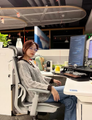 The image shows a young person sitting at a dual-monitor trading setup, appearing focused on the screens, which visually represents the MIT student referenced in the post who uses Claude to backtest BTC trading strategies—his relaxed posture at the workstation symbolizing how the AI tool has automated much of the analytical work behind his reported $830,000 profit.