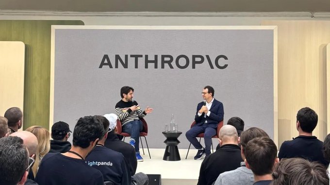 Two men sit on stage in conversation beneath a large "ANTHROPIC" backdrop at what appears to be a corporate or investor event. The image visually supports the post's announcement about Anthropic's massive $2 trillion valuation discussions by showing the company's public-facing presence.